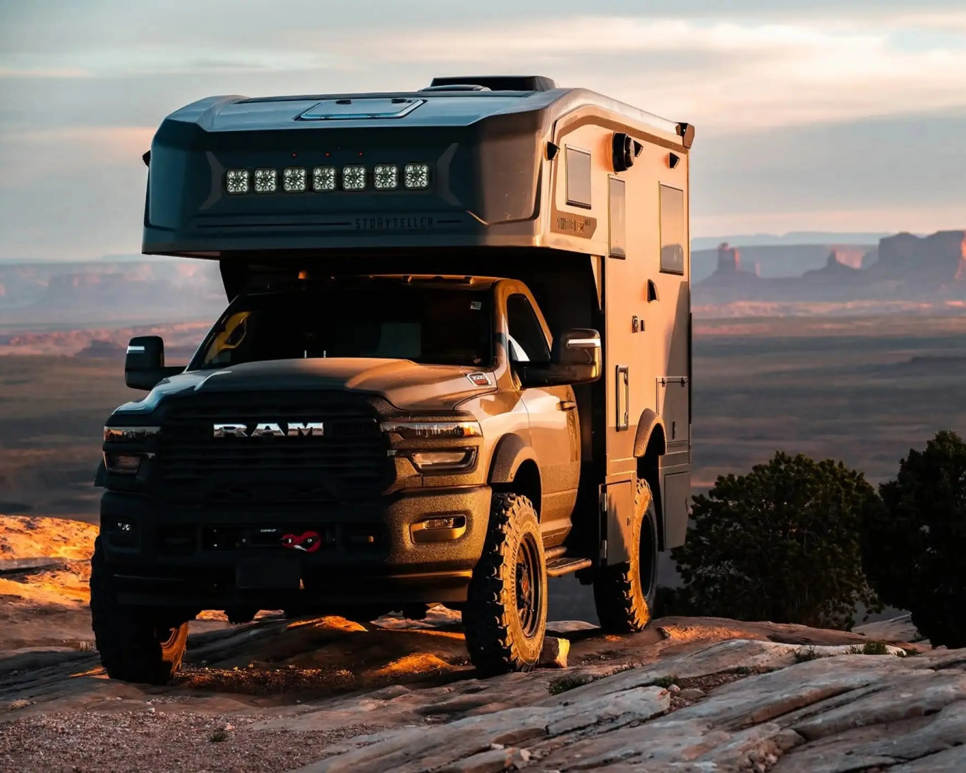 Black RAM truck with off-road camper parked on rocky terrain at sunset.