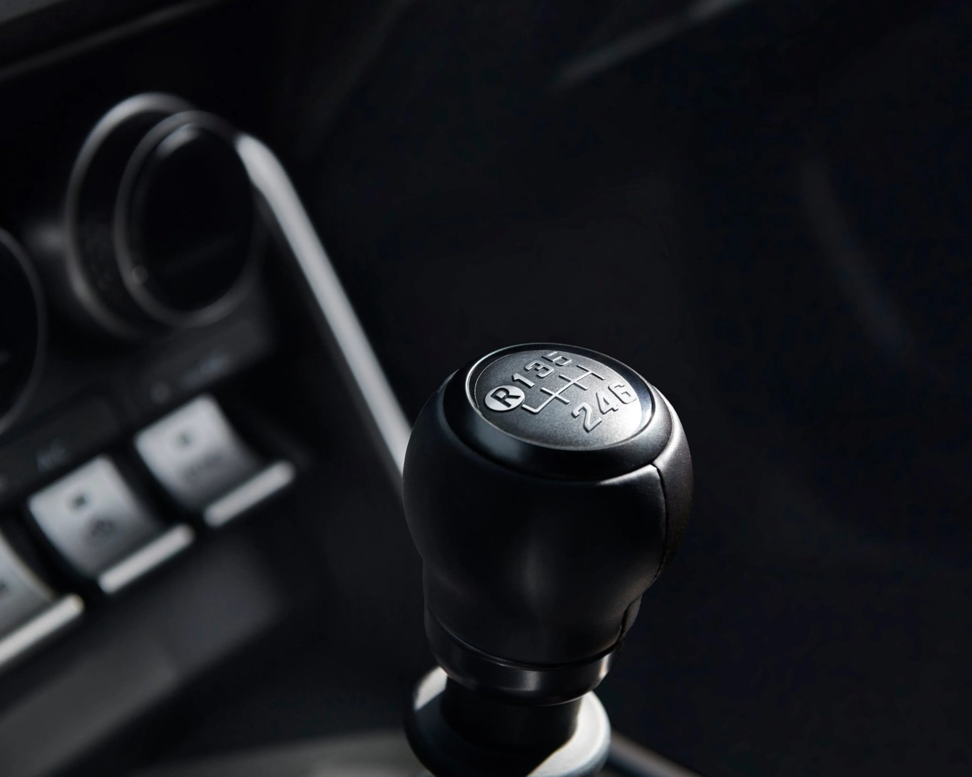 Black manual gear shift knob with silver top showing six-speed pattern and reverse gear in a car interior.