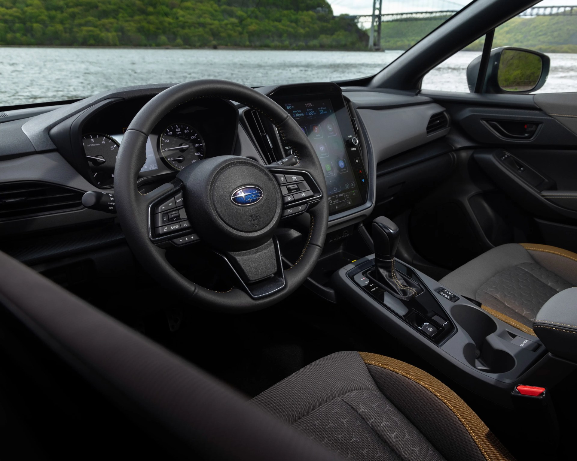 Interior of a Subaru car showing a black leather steering wheel with controls, digital touchscreen, and fabric seats with brown accents.