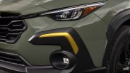 Close-up of a green car front with black grille, angular headlight, yellow accent on black bumper, and fog light.