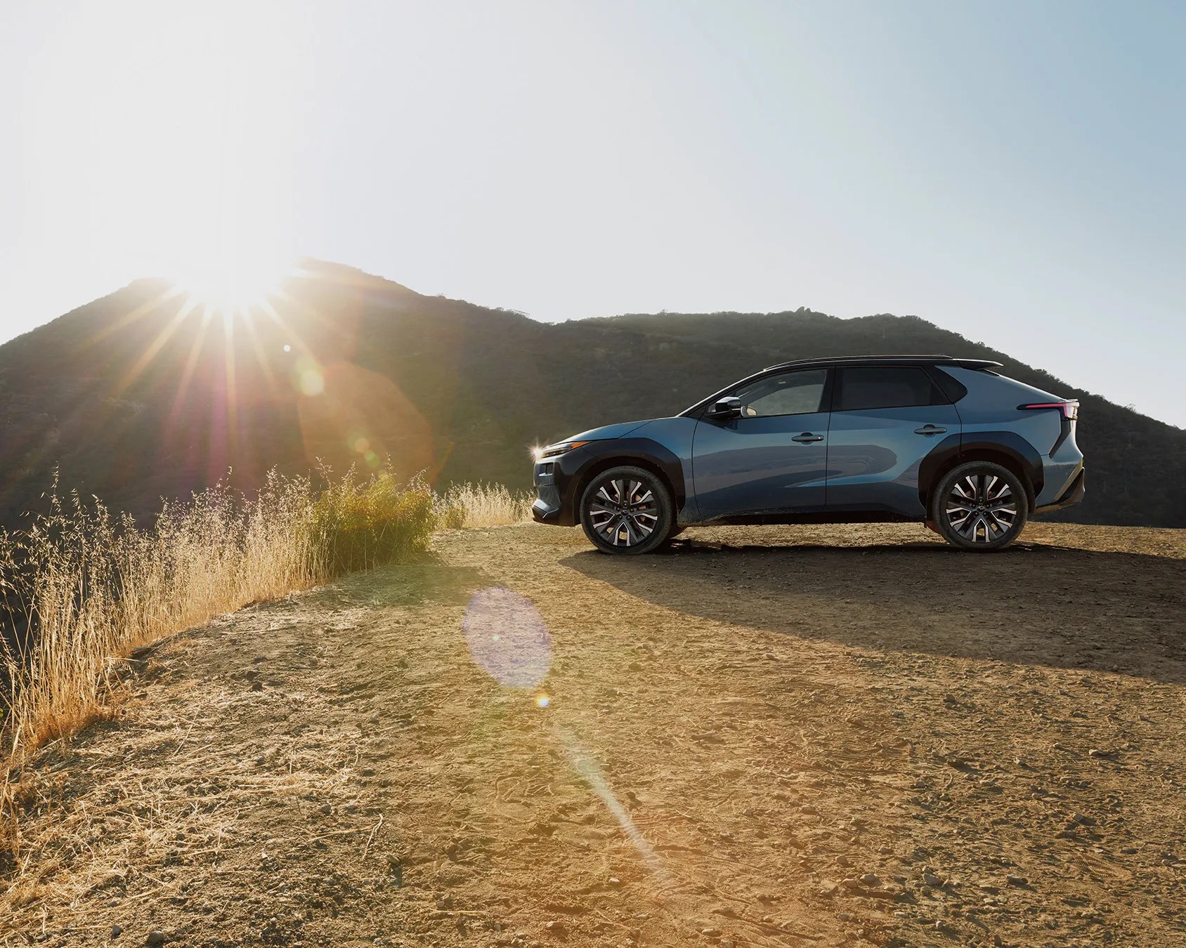 Blue crossover SUV parked on a dirt trail with sunlit hills in the background.