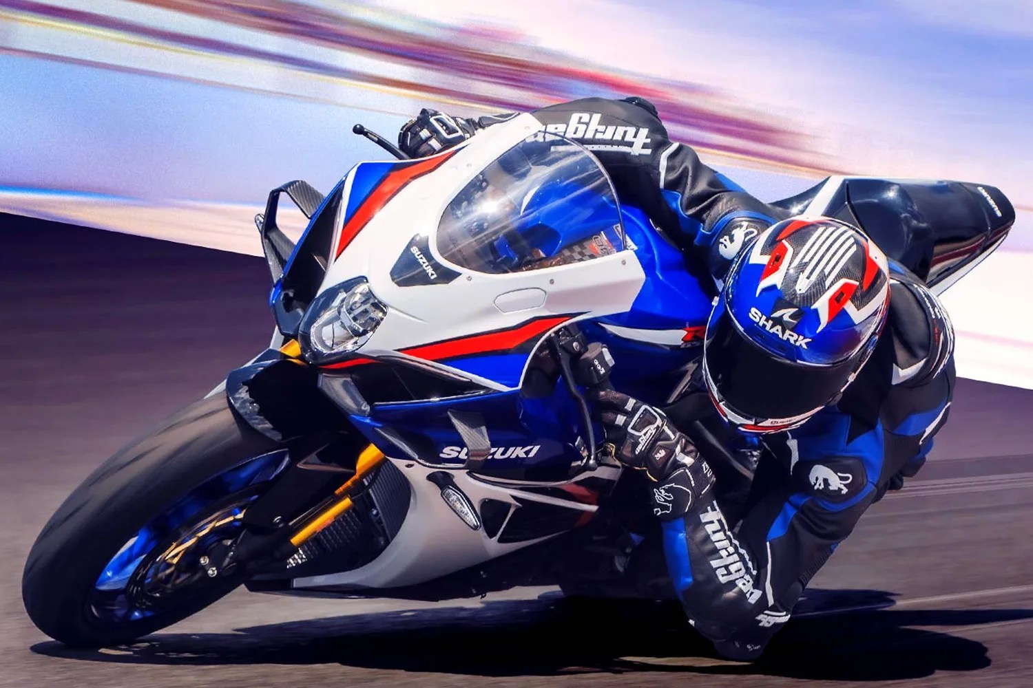 Rider in black and blue racing suit leaning into a turn on a blue, white, and red Suzuki sport motorcycle.