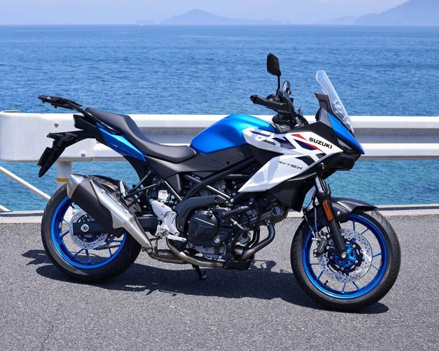 Blue and white Suzuki SV650X motorcycle parked on a road by the ocean.