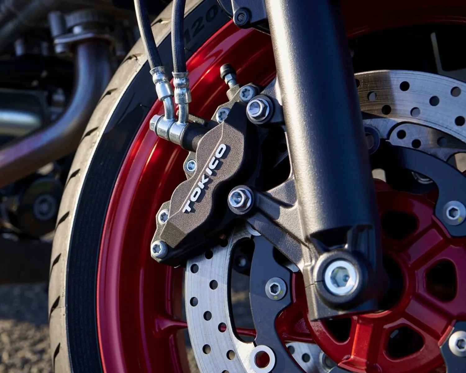 Close-up of a red motorcycle wheel with a silver perforated brake disc and a black Tokico brake caliper.