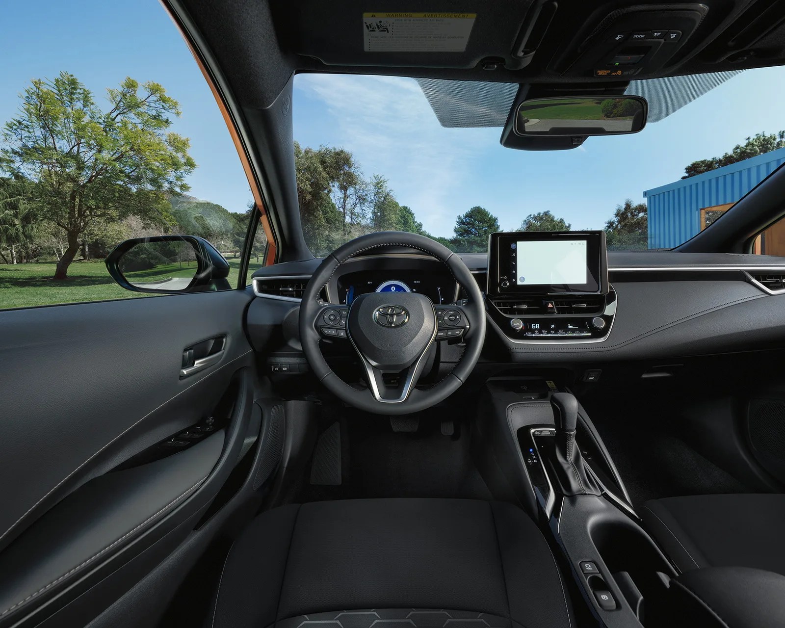 Interior view of a Toyota car showing a black steering wheel, digital dashboard, touchscreen display, and gear shift.