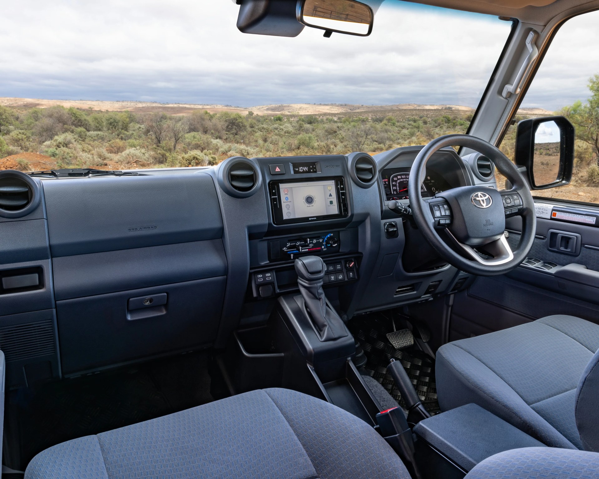 Interior of a right-hand drive Toyota Land Cruiser with blue fabric seats and a touchscreen display.