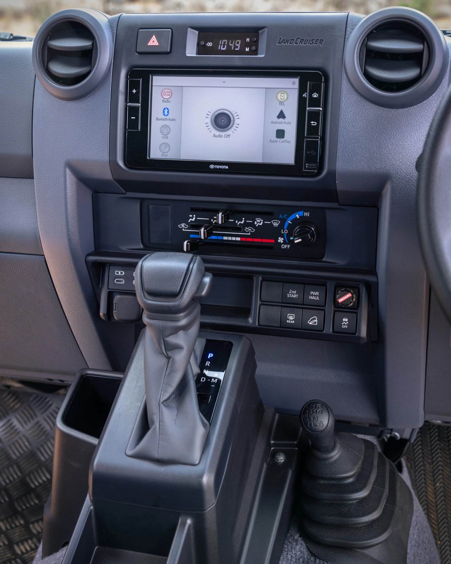 Center console of a Toyota Land Cruiser showing gear shifters, climate controls, and touchscreen infotainment system.