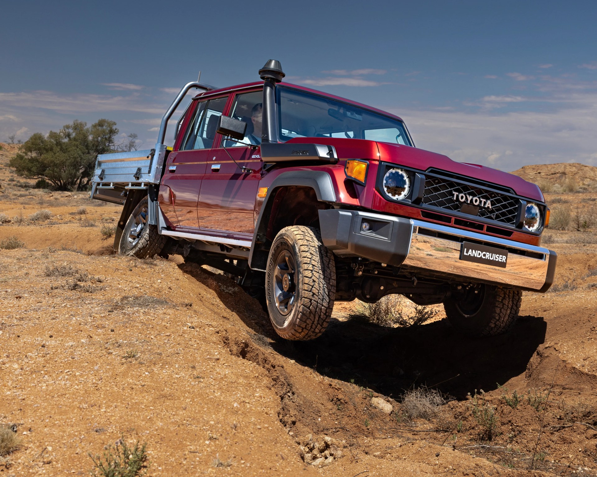 Red Toyota Land Cruiser pickup truck with snorkel driving off-road on a dirt trail.