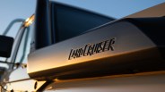 Close-up of a black Land Cruiser roof rack with embossed lettering, illuminated by warm sunlight.