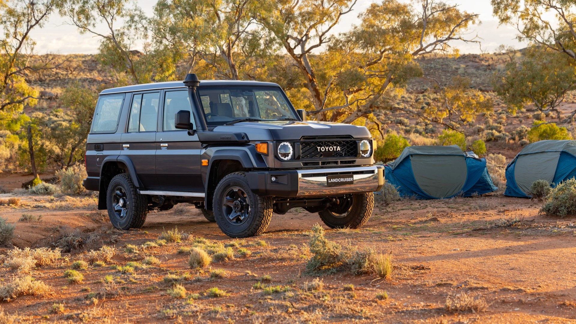 Dark gray Toyota Land Cruiser parked on dry terrain with two blue and gray tents in the background.