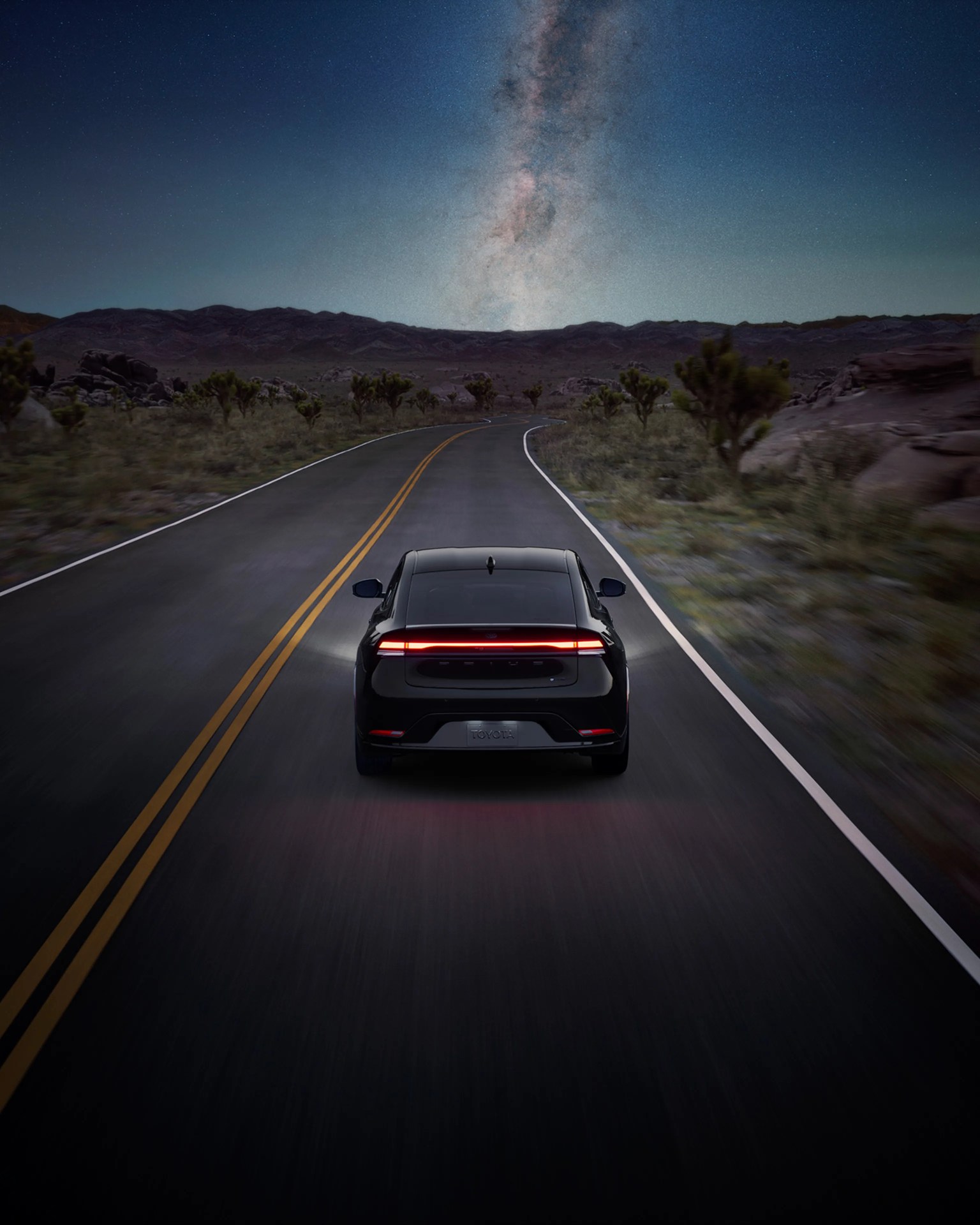 Black Toyota electric SUV driving on a desert road under a starry night sky with the Milky Way visible.