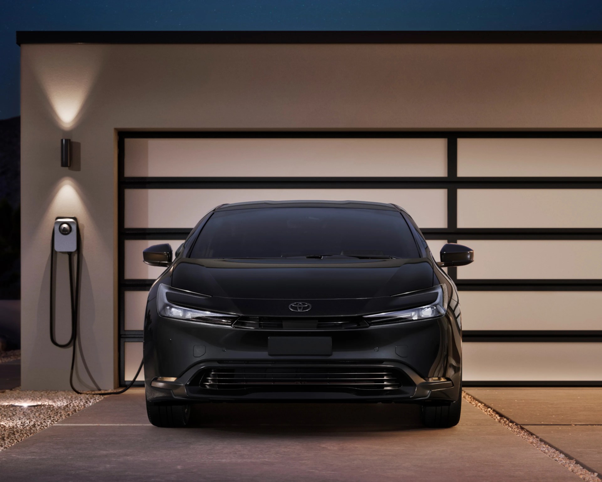 Black Toyota electric car parked in front of a modern garage with a wall-mounted EV charger.