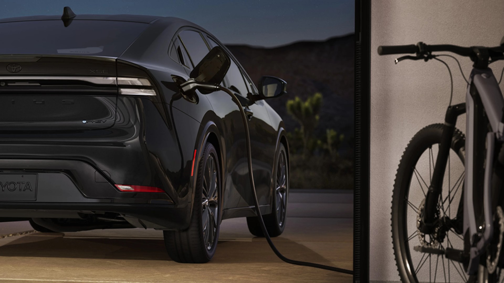 Black Toyota electric vehicle charging at a home garage with a bicycle partially visible on the right.