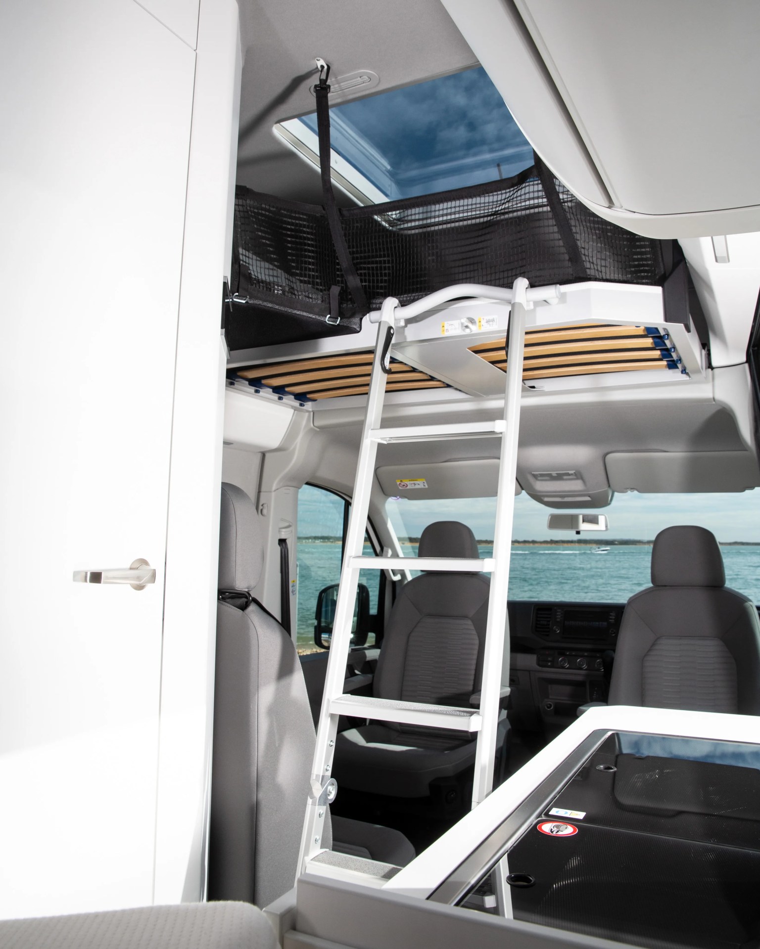 White ladder leading to a loft bed with wooden slats and black safety netting inside a camper van.