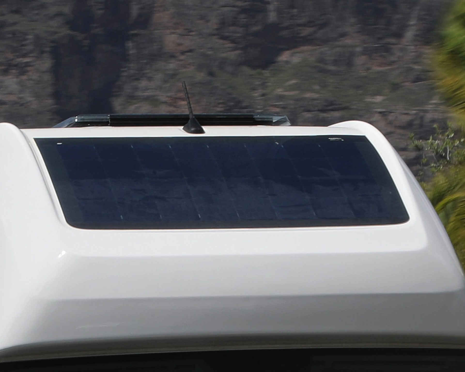 Black solar panel mounted on the white roof of a vehicle with an antenna and a roof vent.