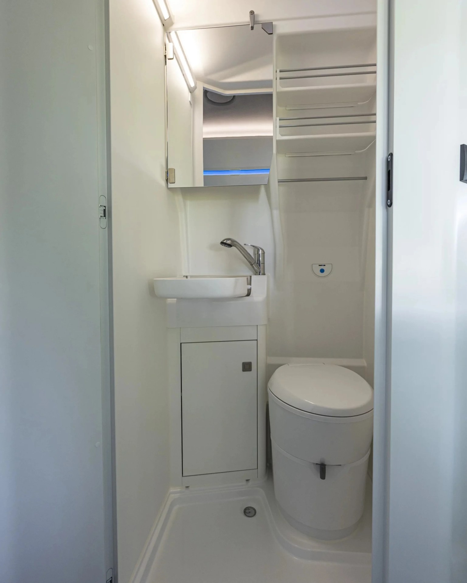 Compact white bathroom with a small sink, mirror cabinet, and a toilet in a confined space.