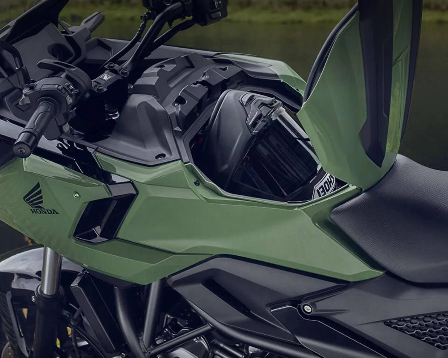 Green Honda motorcycle with open front storage compartment containing a black helmet.