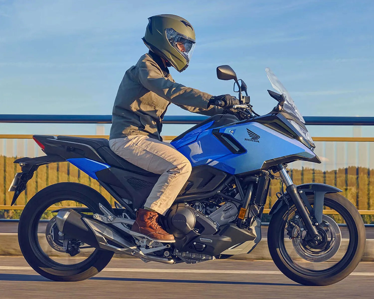 Person wearing a green helmet and brown boots riding a blue Honda motorcycle on a road.