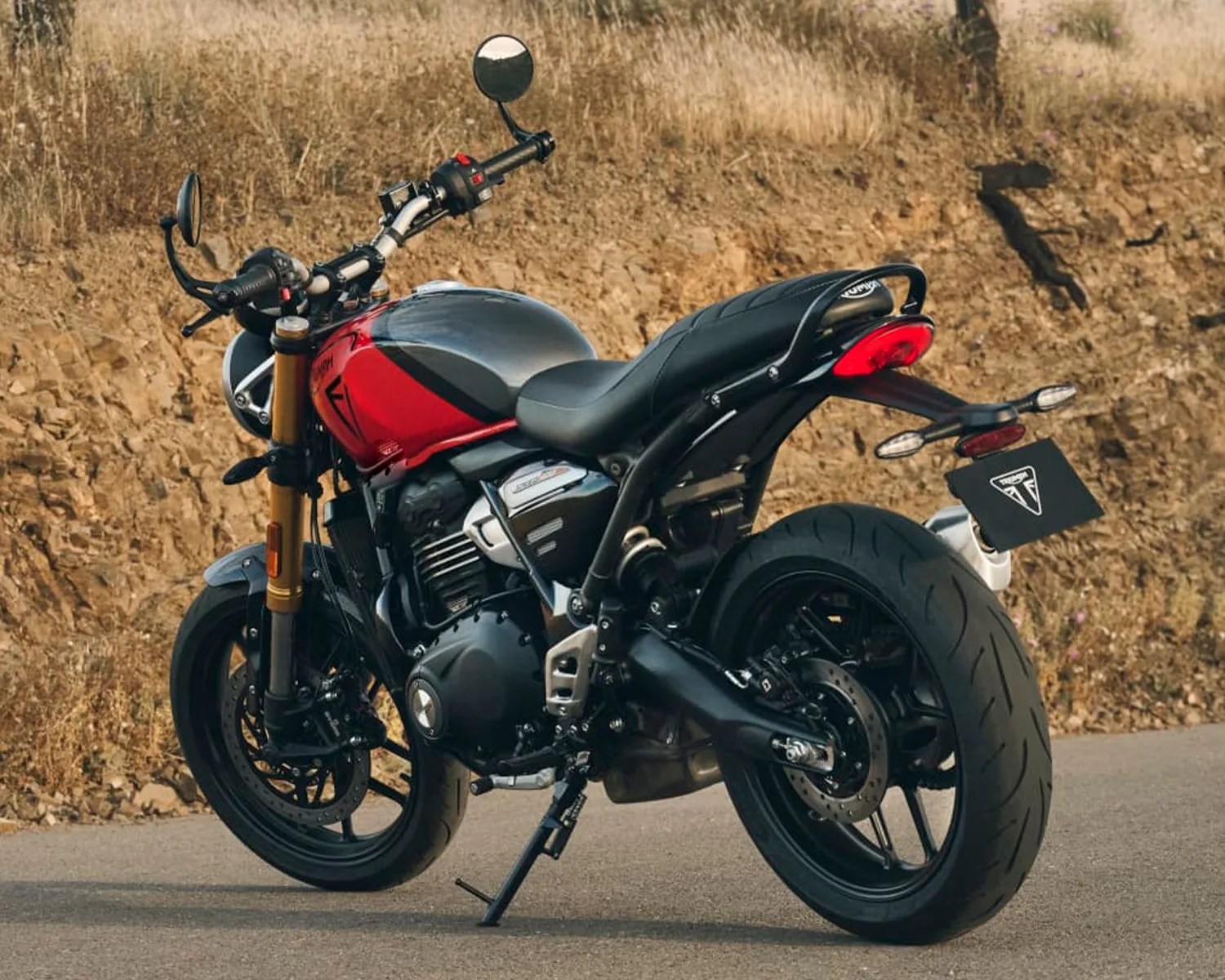 Black and red Triumph motorcycle parked on a road with dry grass in the background.