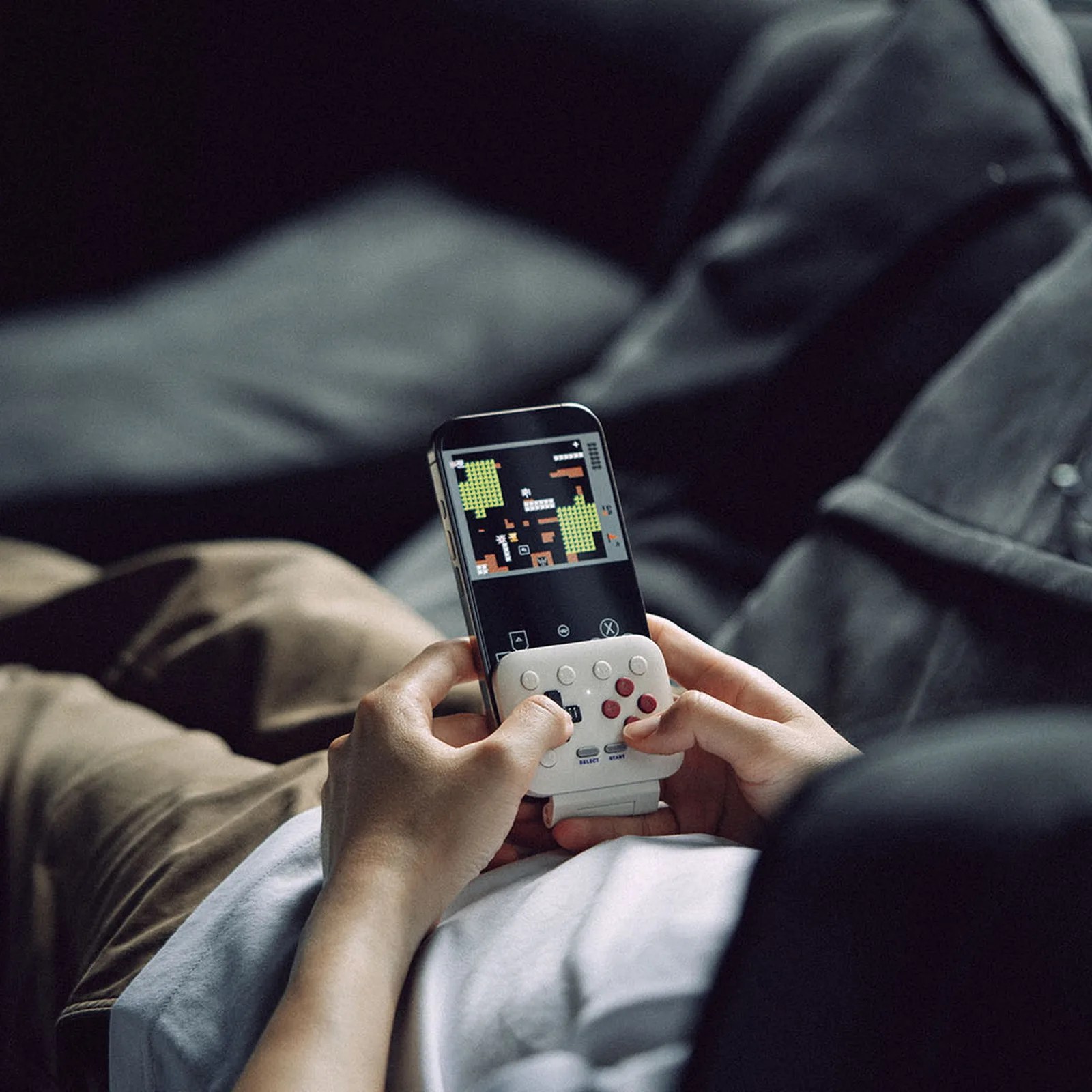 Person holding a black handheld gaming device with a white detachable controller playing a pixelated game.
