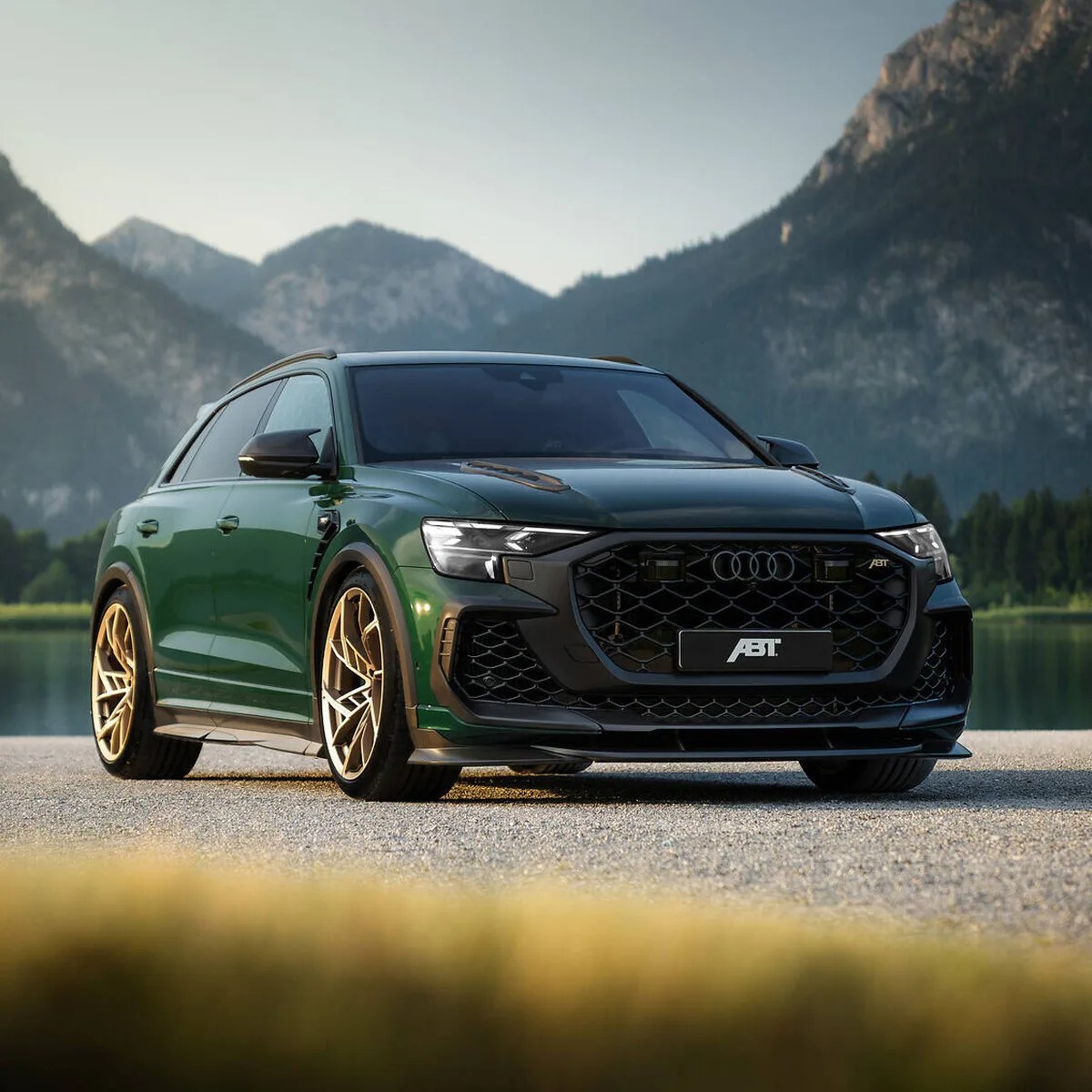 Dark green Audi SUV with black grille and gold alloy wheels parked on gravel with mountains in the background.