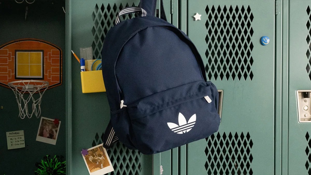 Navy blue Adidas backpack with white trefoil logo hanging on a green locker.