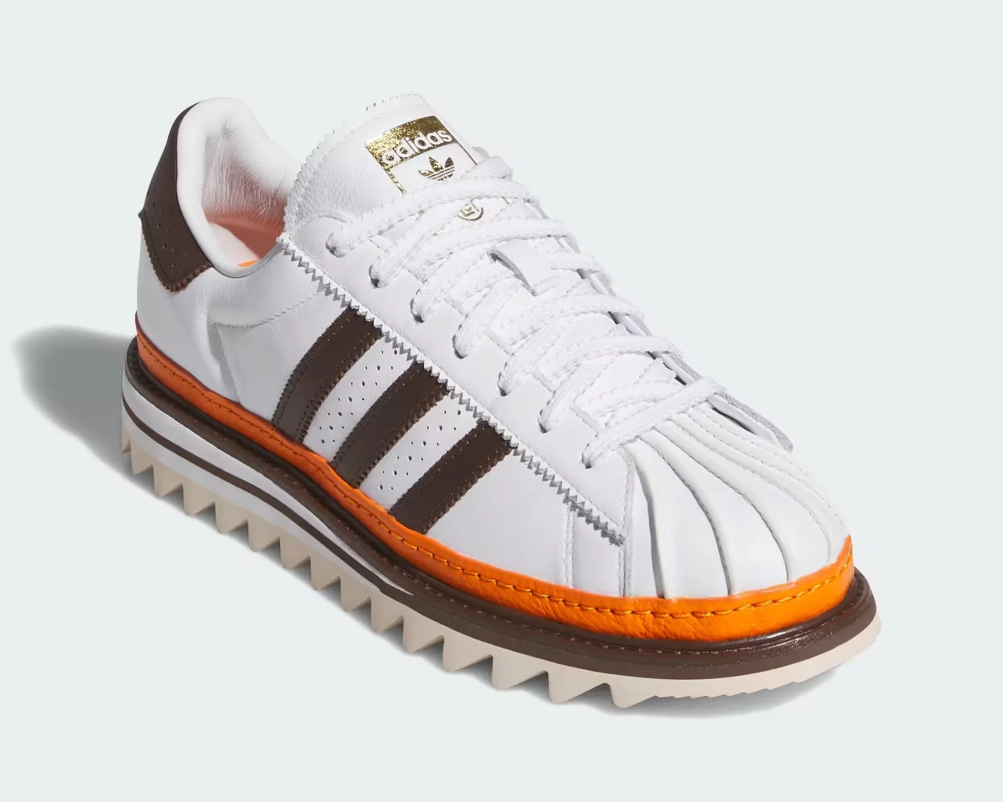 White Adidas sneaker with brown stripes, orange trim, and a jagged beige sole.