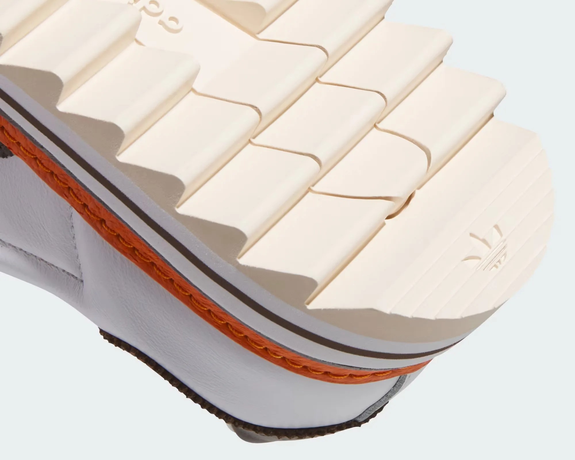 Close-up of a cream-colored shoe sole with deep grooves and orange stitching on white leather upper.
