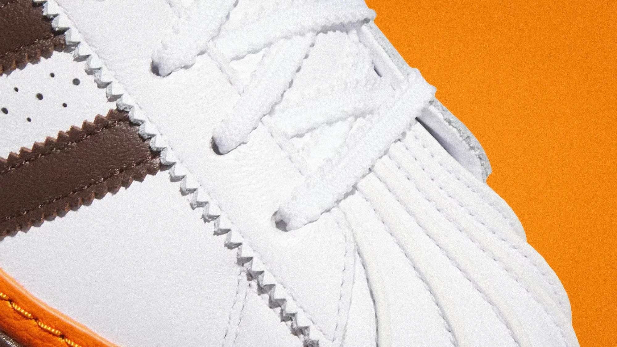 Close-up of a white sneaker with brown leather stripes and white laces on an orange background.
