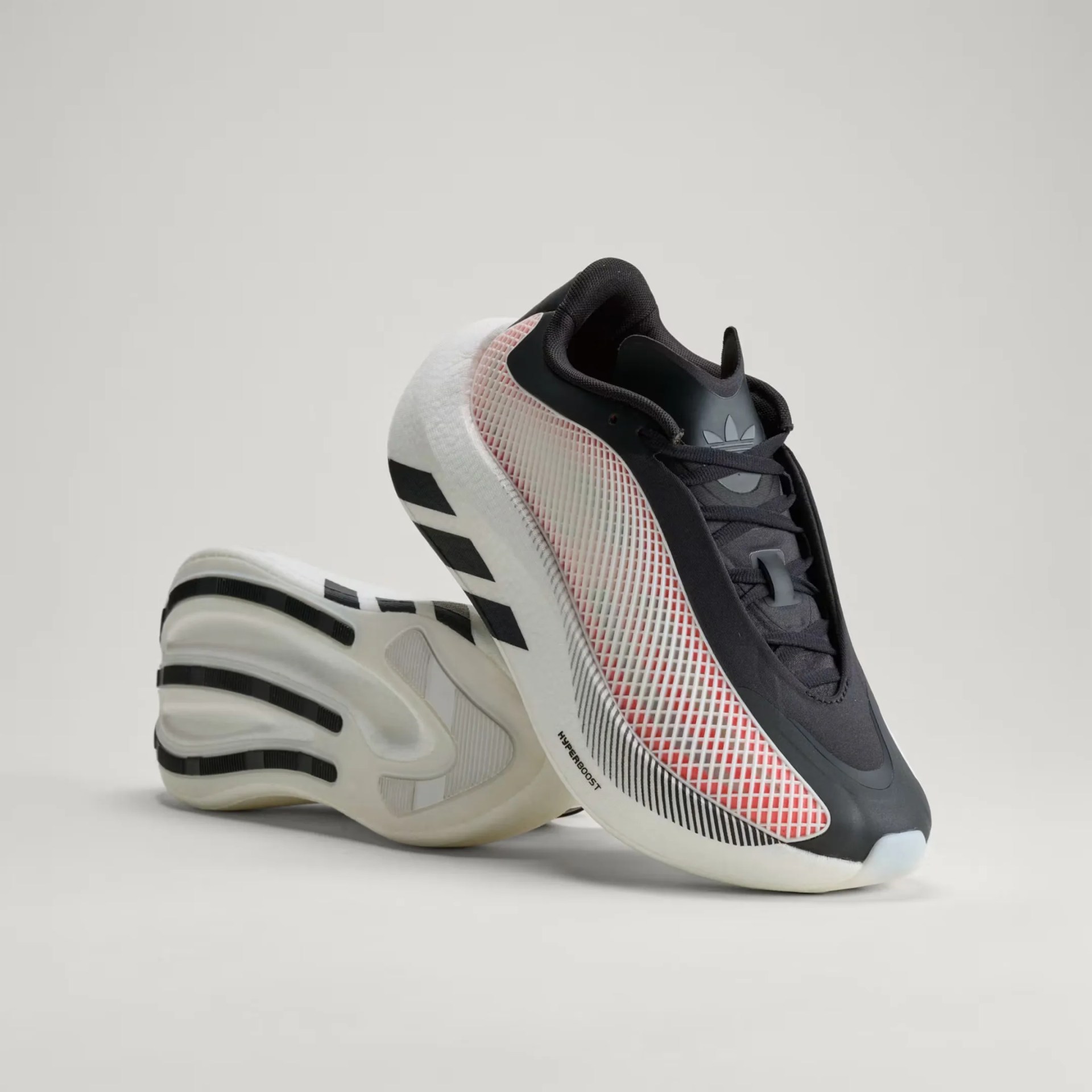 Pair of black and white Adidas Hyperboost sneakers with red mesh side panels on a gray background.