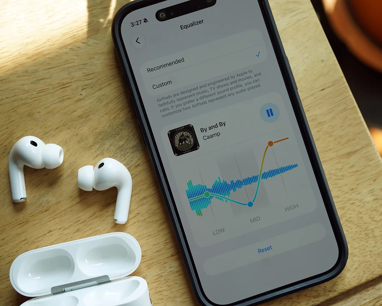 Smartphone displaying an equalizer screen with AirPods and an open charging case on a wooden surface.