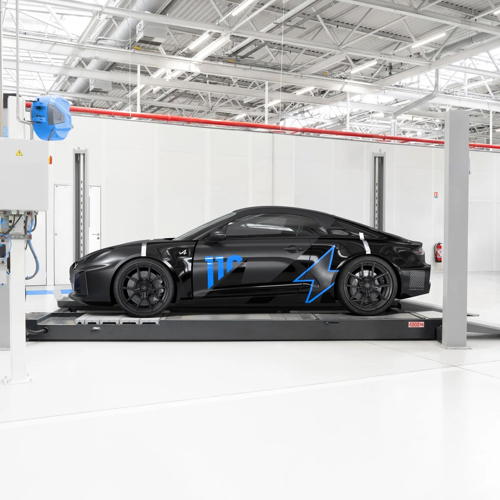 Black sports car with blue "110" and star graphics on the side, parked in a bright industrial garage.