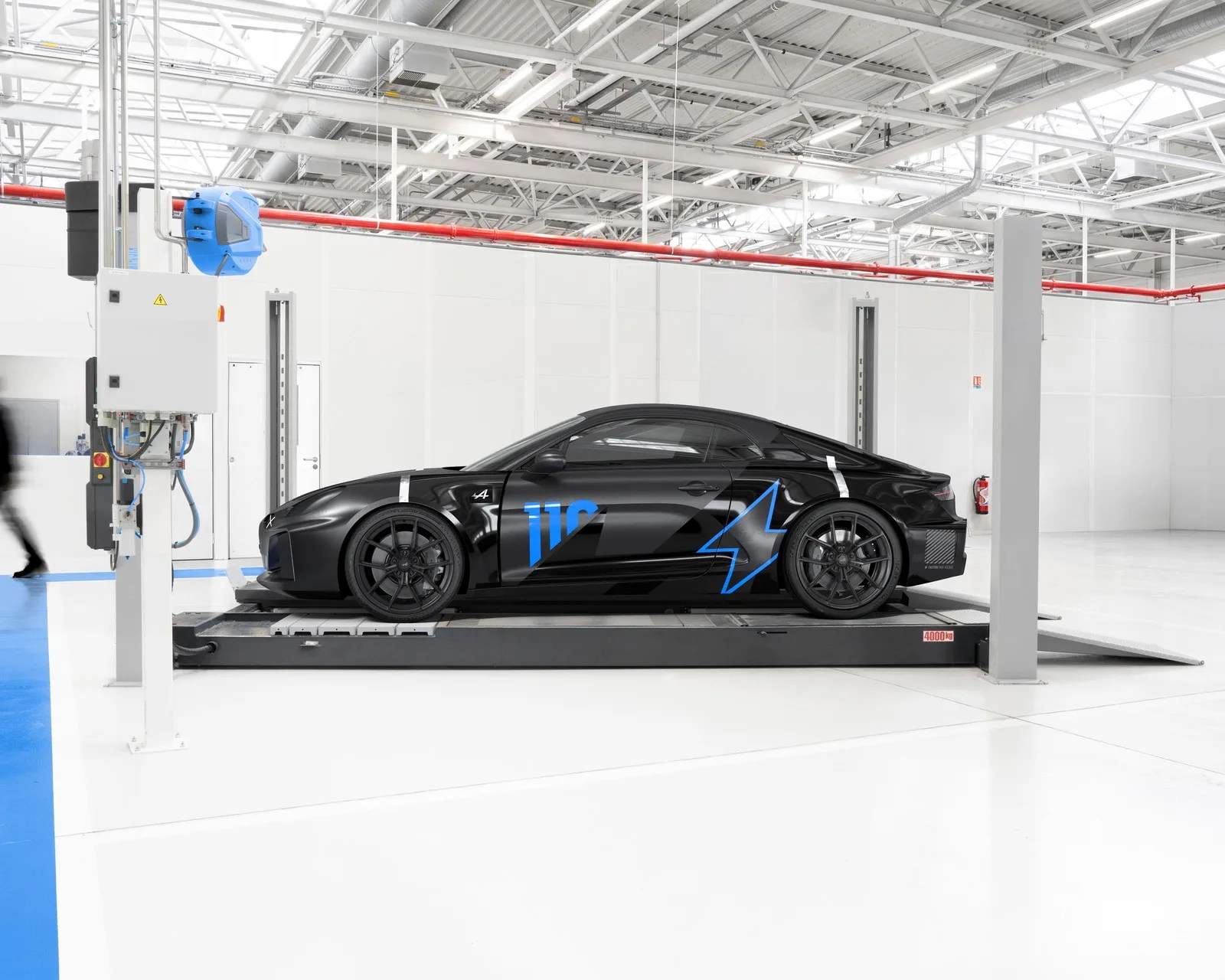 Black sports car with blue lightning bolt and number 110 decals on a platform in a bright white garage.