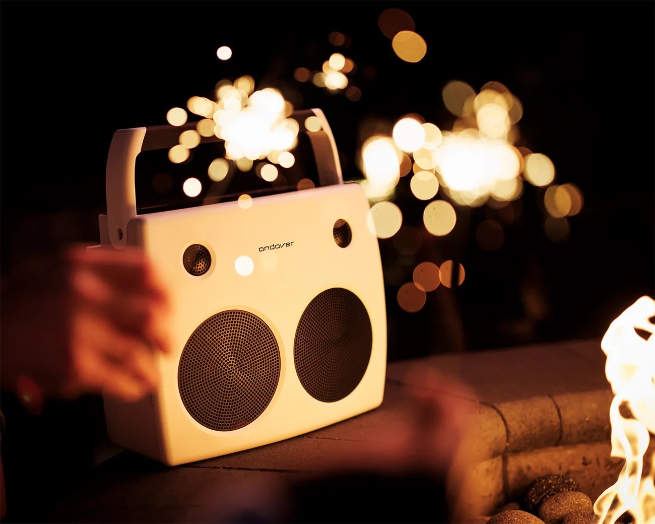 White portable speaker with two large black speaker grilles and a handle, glowing lights in the background.