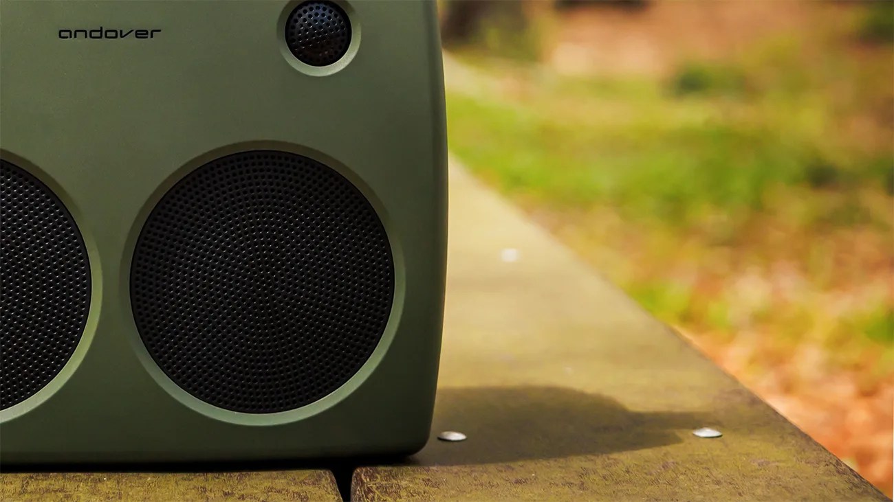 Green Andover portable speaker with black speaker grills on a wooden surface outdoors.