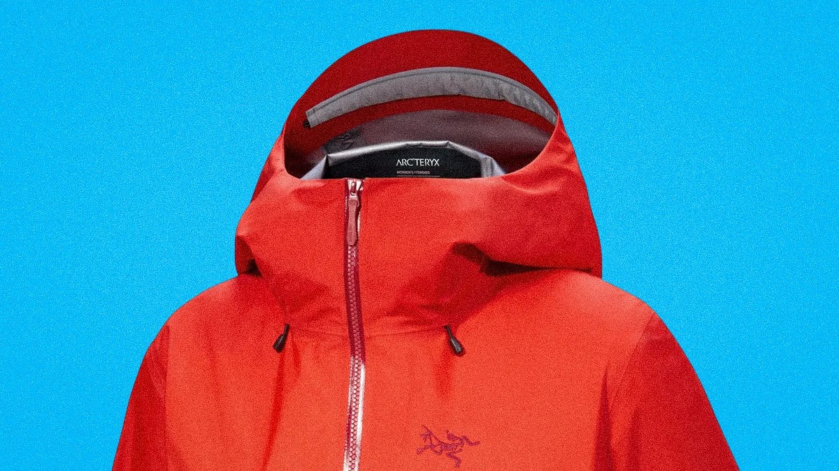 Red Arc'teryx waterproof jacket with a hood against a blue background.