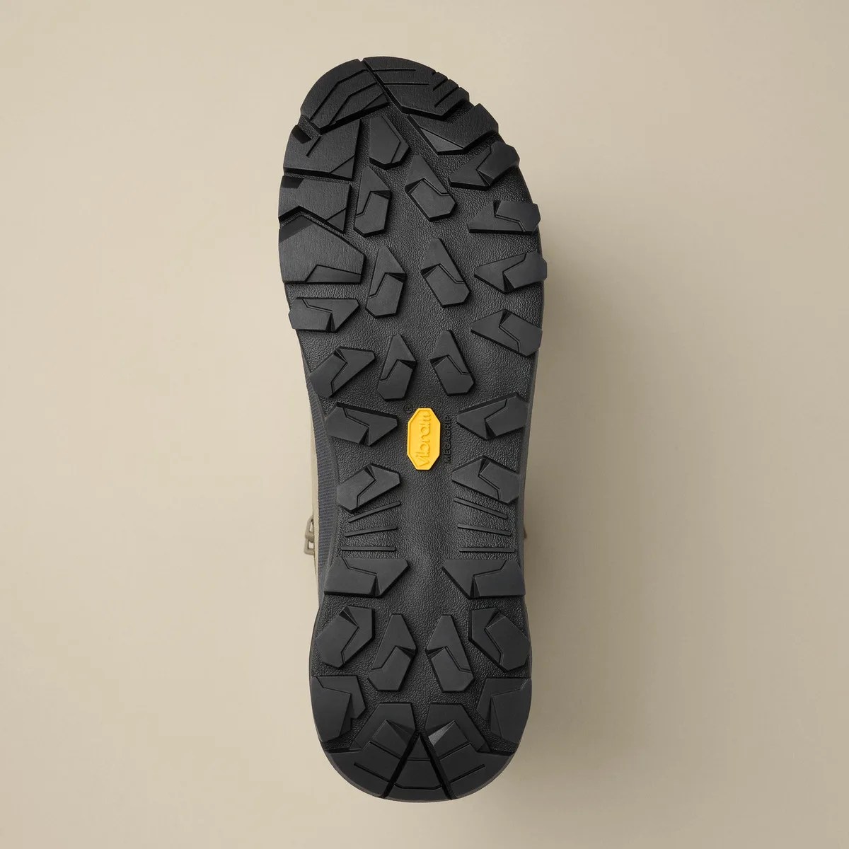Black Vibram Megagrip rubber sole with deep lugs for traction on a beige background.