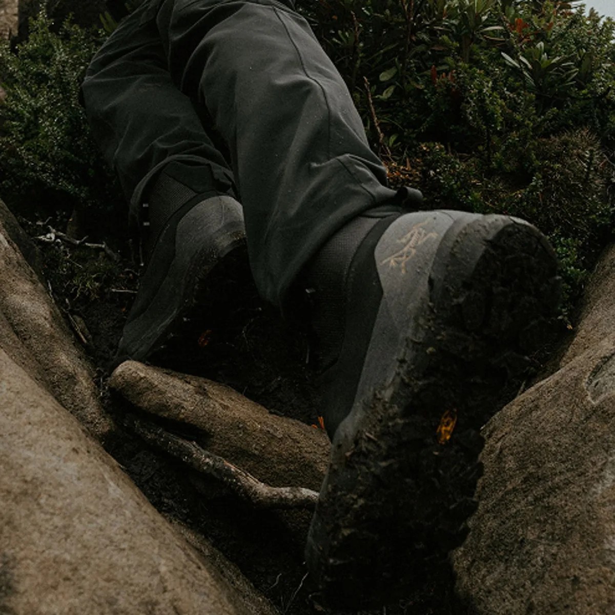 Black hiking boots with rugged soles worn by a person climbing over rocks and moss.