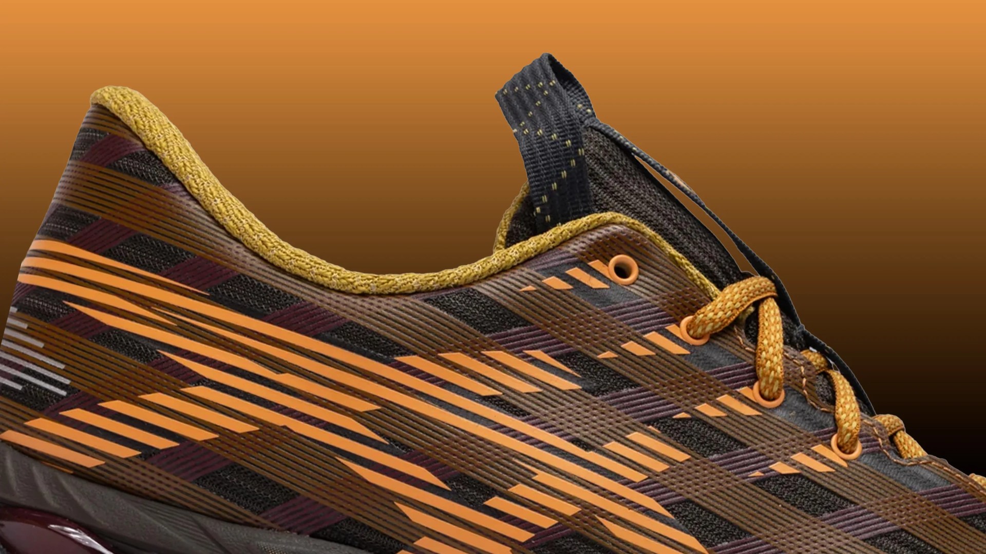 Close-up of a brown and orange athletic shoe with yellow laces and a black pull tab.