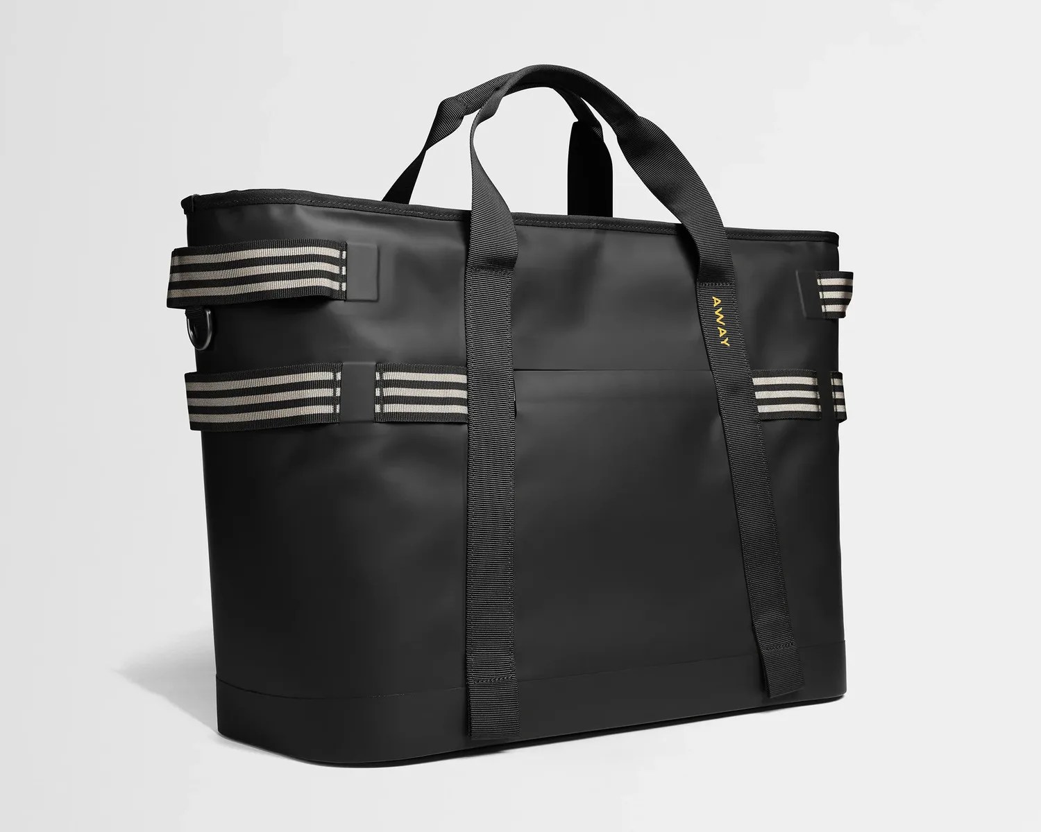 Black rectangular tote bag with striped side straps and black handles, featuring the brand name "AWAY" in yellow.