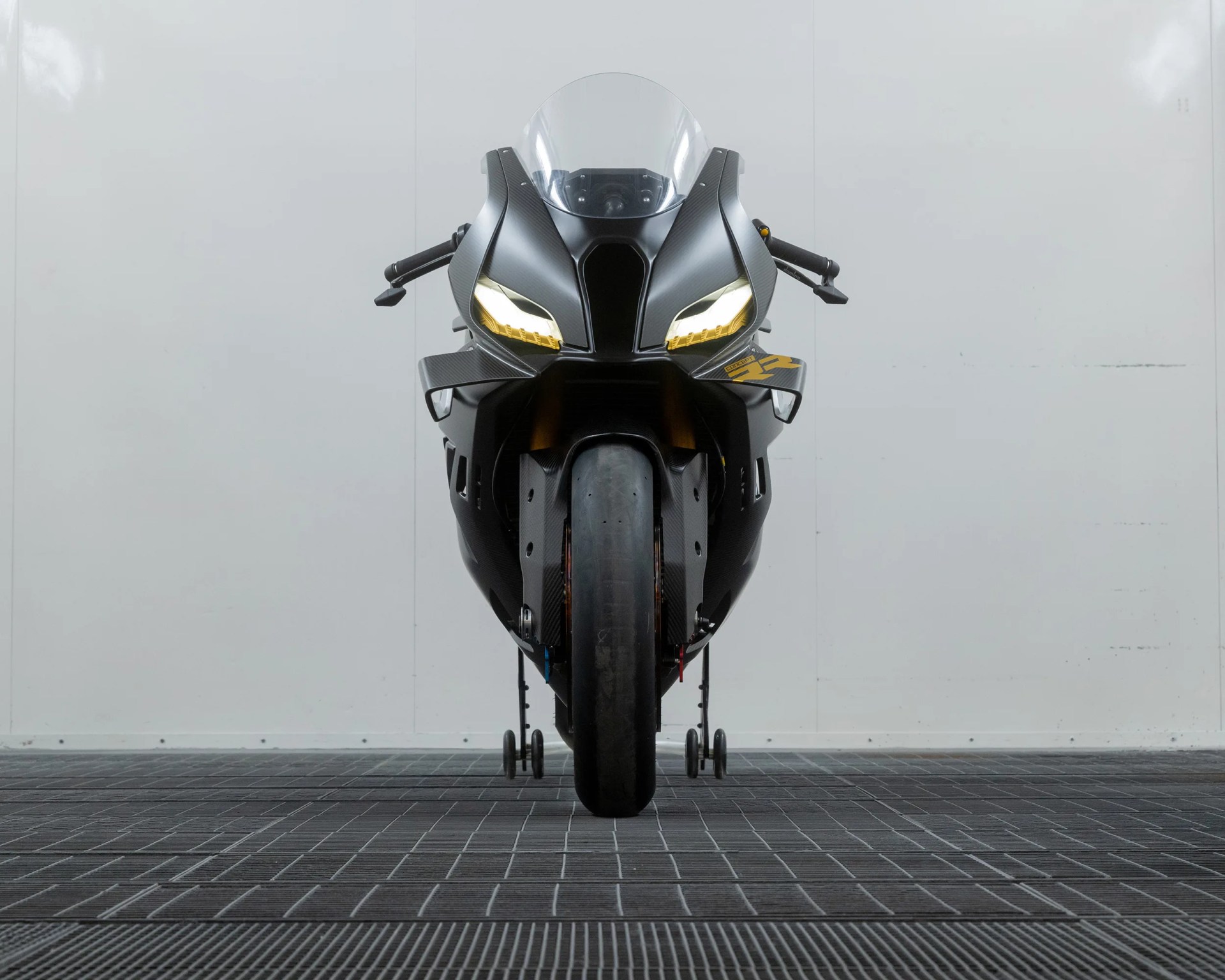 Front view of a black sport motorcycle with yellow-tinted headlights and carbon fiber body panels on a tiled floor.