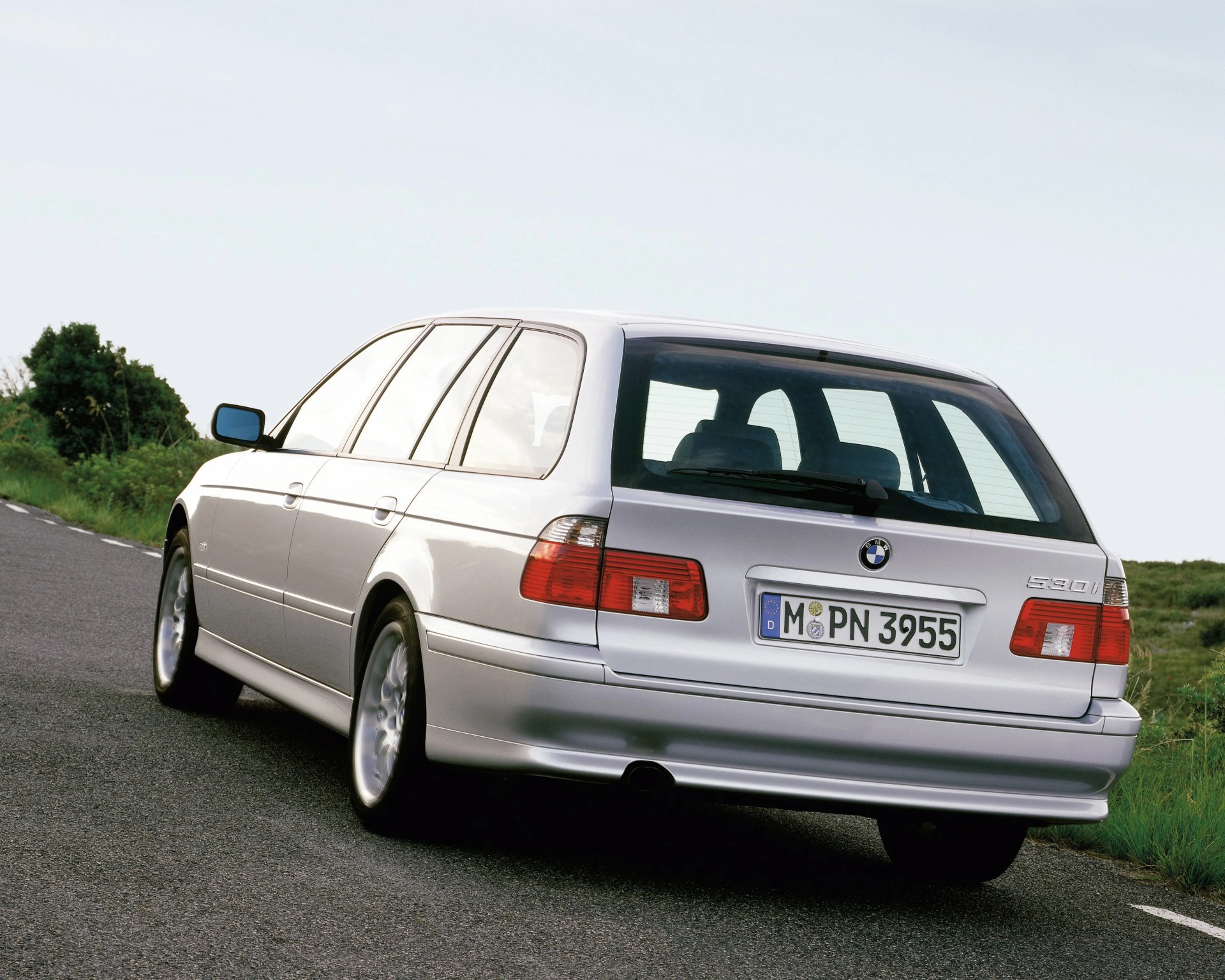 Silver BMW 530i station wagon parked on a road with green bushes in the background.