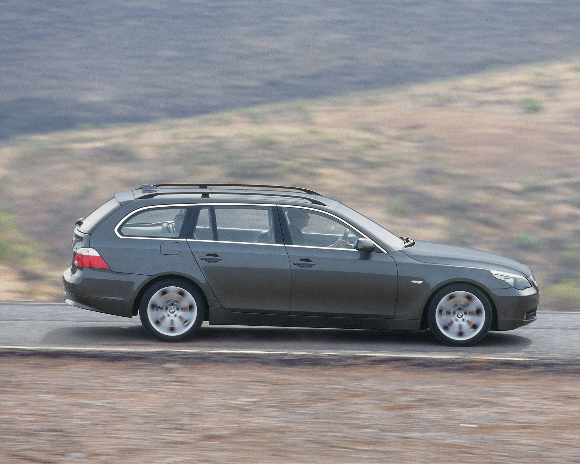 Dark gray BMW station wagon driving on a road with blurred desert landscape in the background.