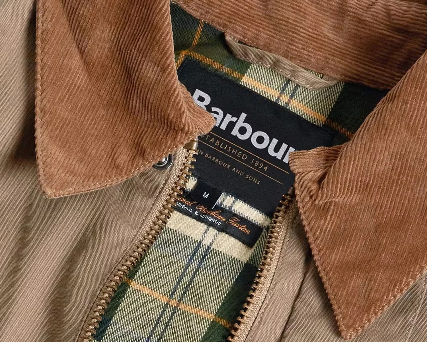 Close-up of a Barbour jacket label with a brown corduroy collar and green plaid lining.