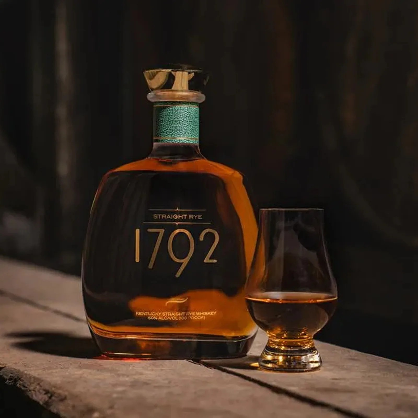Square bottle of 1792 Kentucky Straight Rye Whiskey with amber liquid and a glass of whiskey on a wooden surface.