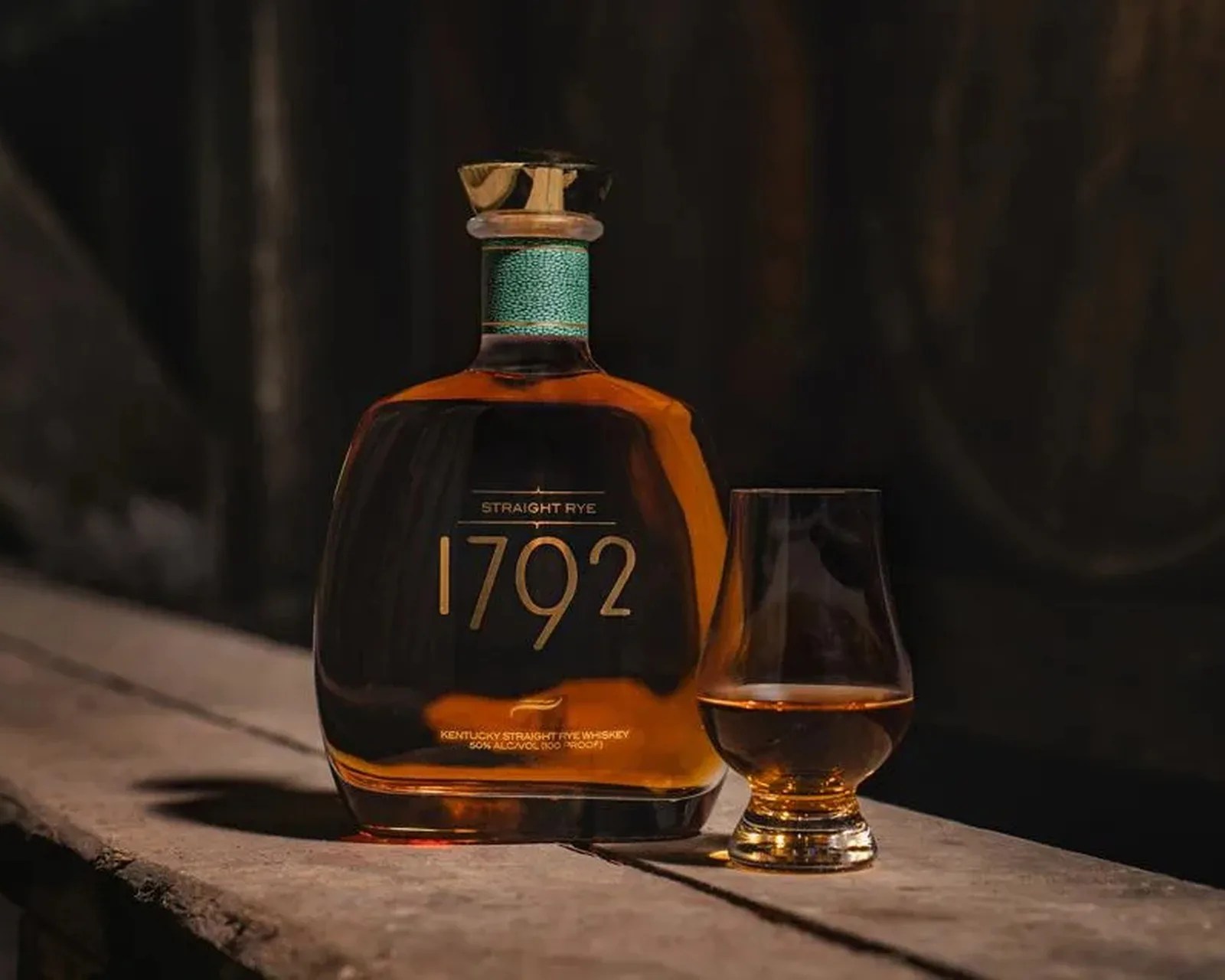 Bottle of 1792 Straight Rye whiskey with a glass of amber whiskey on a wooden surface.
