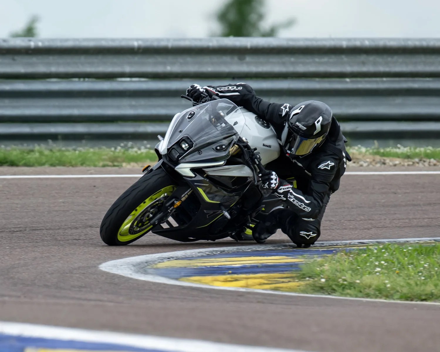 Motorcyclist in black gear leaning into a turn on a white and black Benelli sportbike with neon yellow rims on a racetrack.