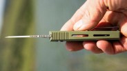 Hand holding a small green folding knife with a thin blade labeled "WORK SHARP.
