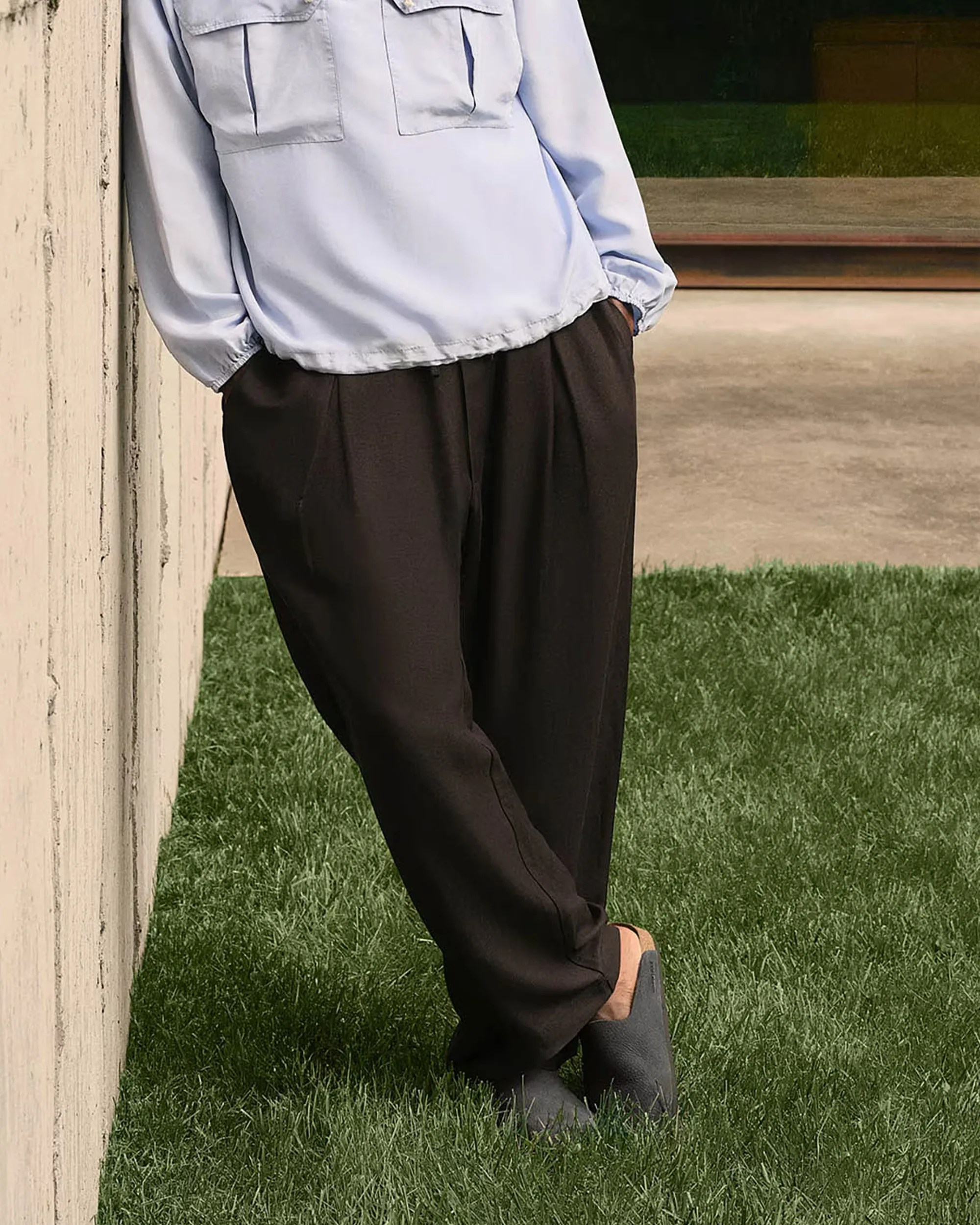 Light blue long-sleeve shirt with chest pockets paired with loose black pants and gray slip-on shoes on grass.