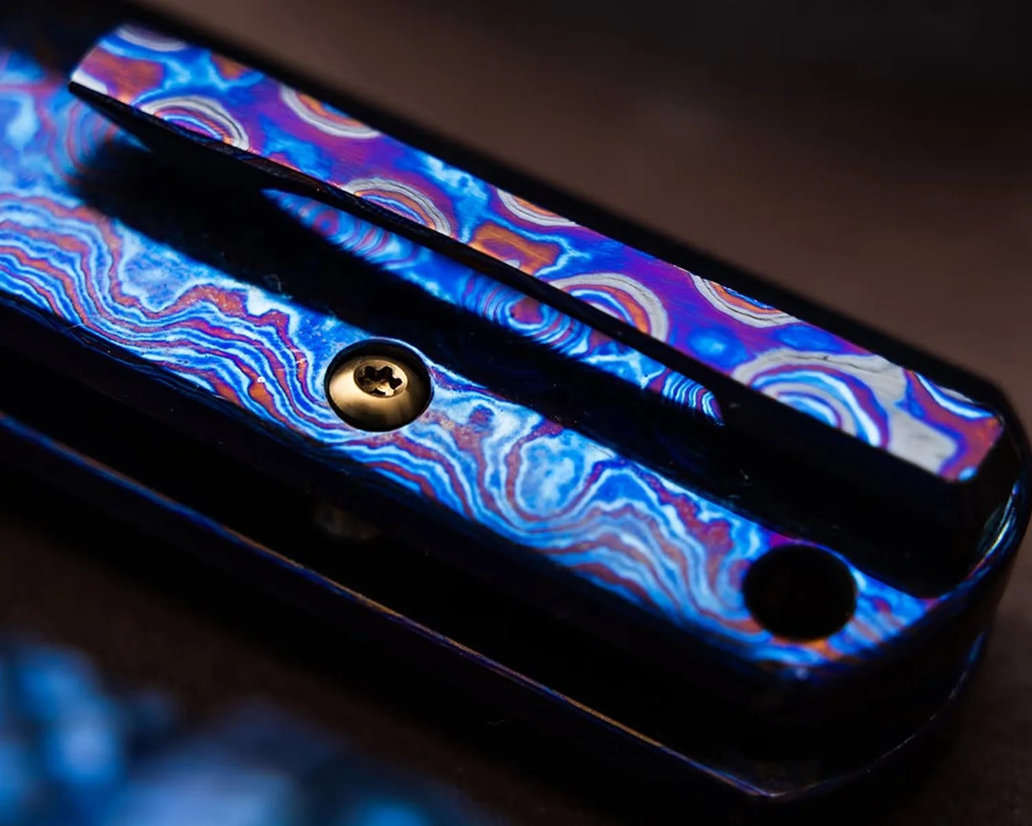 Close-up of a metal object with vibrant blue, purple, and orange swirling patterns and a small brass screw.